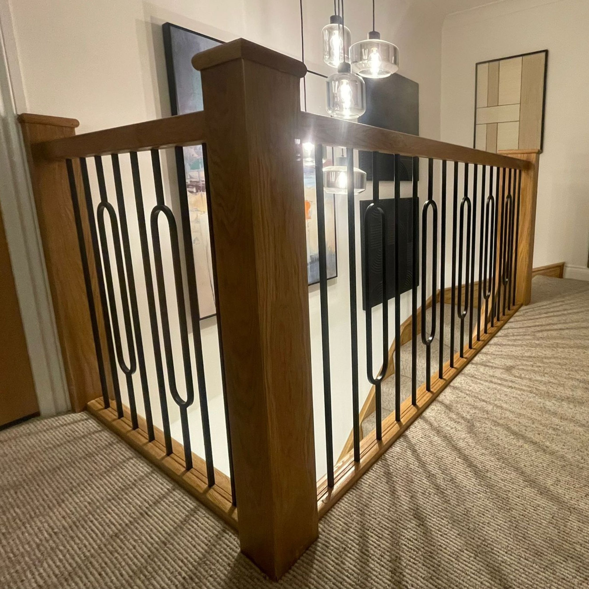 Wood and metal staircase railing next to a bedroom with framed artwork and hanging pendant lights.