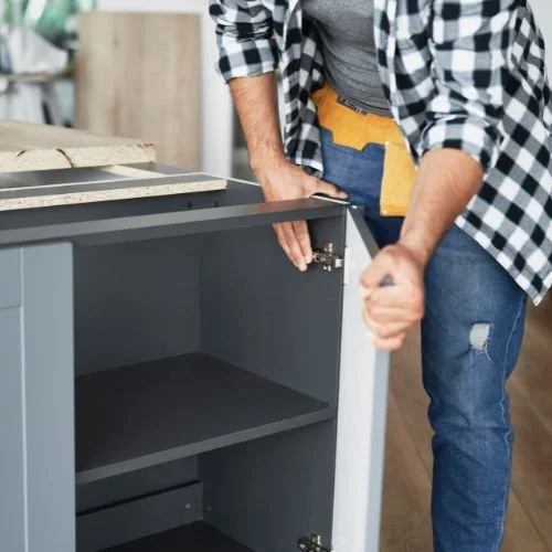 Person assembling or installing a gray cabinet or shelf unit in a home or workshop.