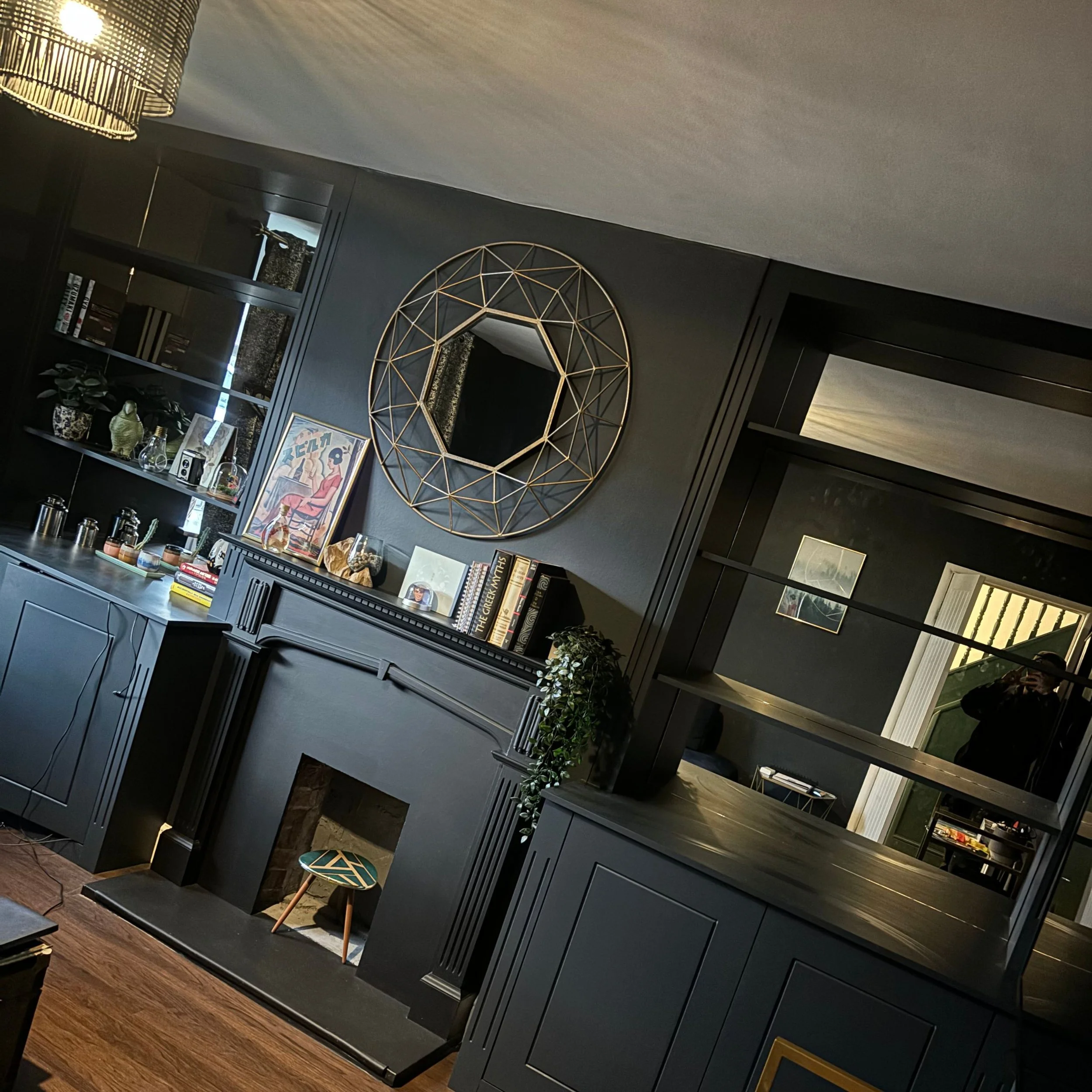 Living room with black walls, black cabinetry, a decorative mirror, books, plants, and a small stool in front of a fireplace.