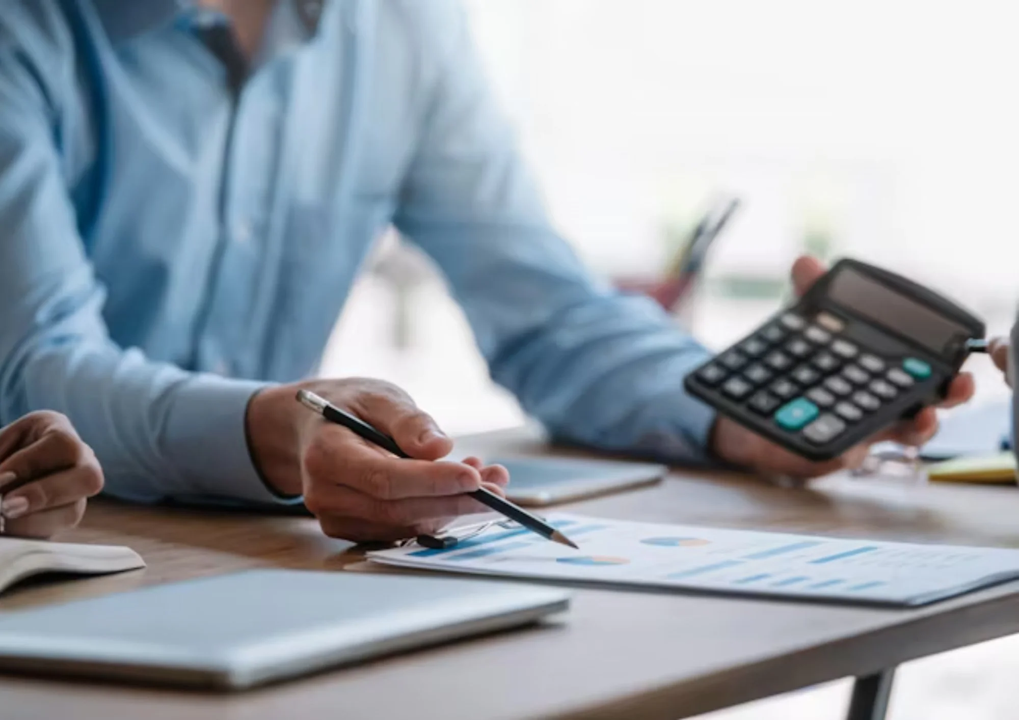 People working on financial documents with a calculator, pen, and notebooks at a desk.