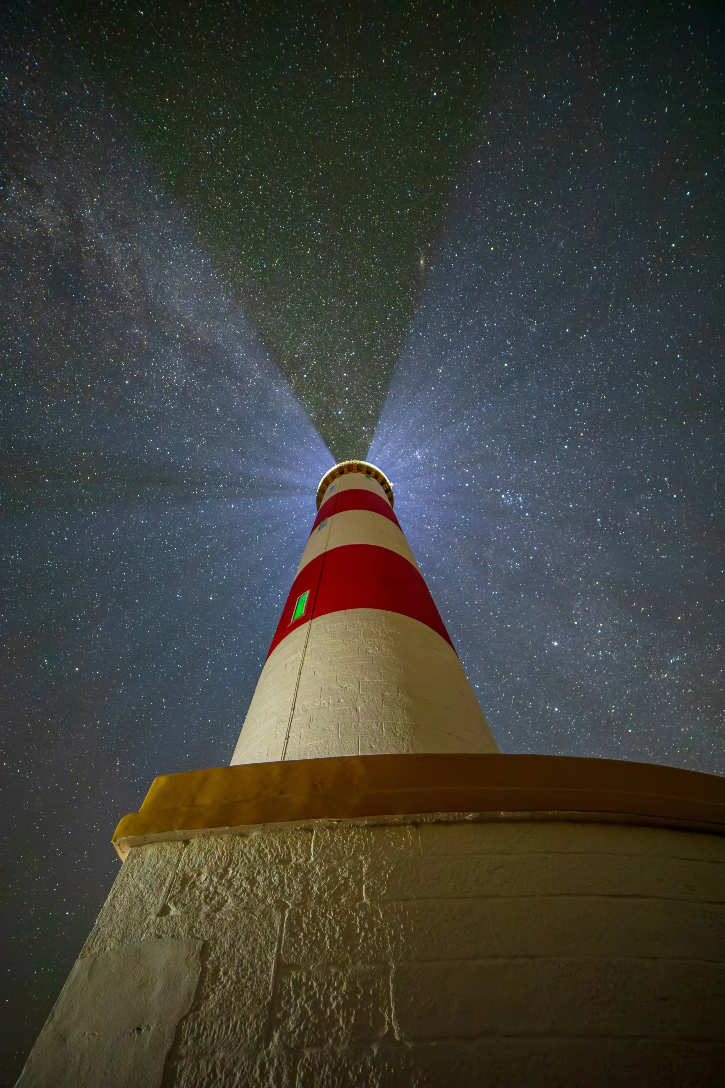 Nighttime view of a lighthouse with its light beaming upward, set against a starry sky.