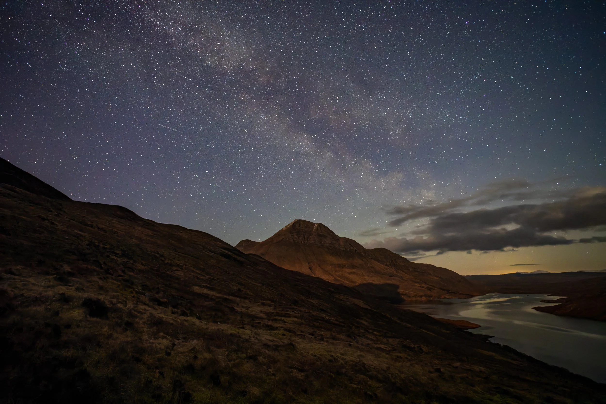 Nighttime landscape of a mountain and river with a starry sky and the Milky Way