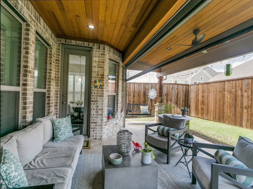 Covered outdoor patio with seating, a brick wall, and a garden with a wooden fence.