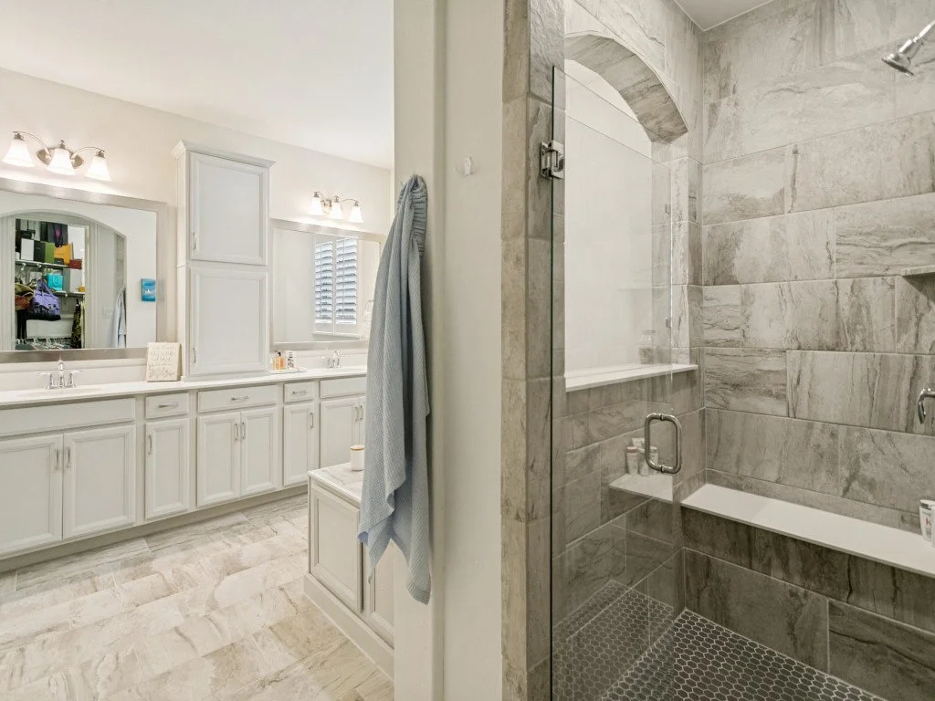 A bathroom with a large vanity and mirror on the left, and a separate walk-in shower with gray tiles on the right.