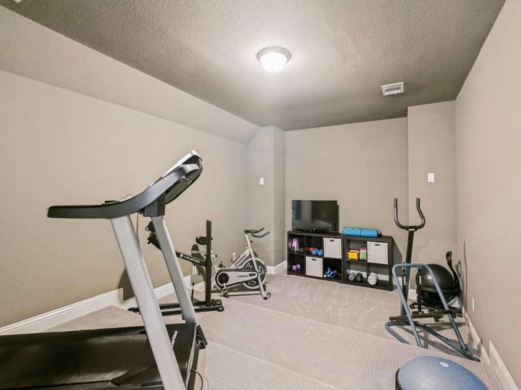 Home gym room with treadmill, stationary bike, exercise ball, small black shelving unit with workout equipment, and a television.
