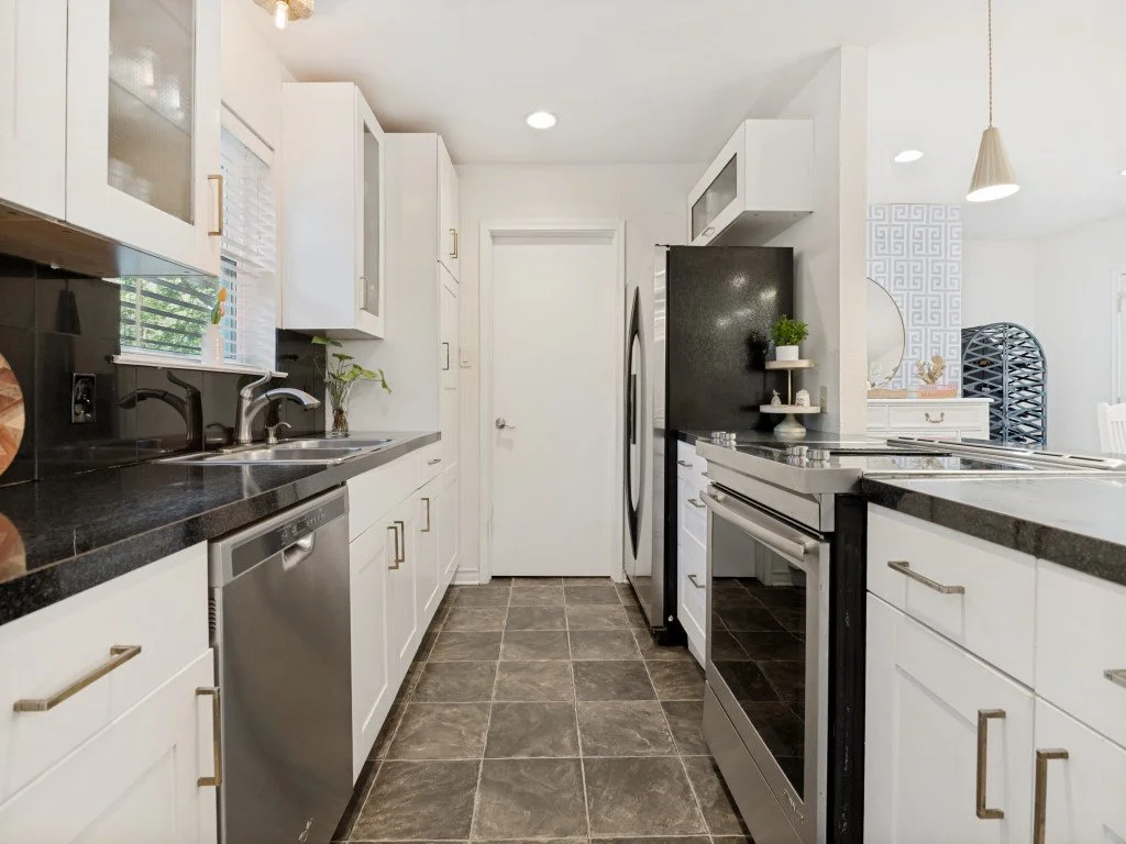 Modern white kitchen with black countertops, stainless steel appliances, and dark tile flooring.