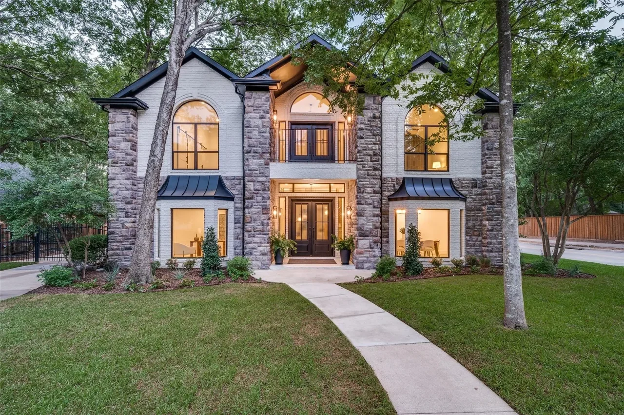 A modern two-story house with stone and brick exterior, large arched windows, and a black front door, surrounded by a well-maintained lawn and trees.