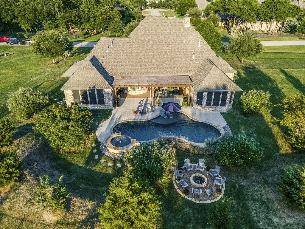 An aerial view of a backyard with a swimming pool, hot tub, outdoor seating area, and surrounding trees.