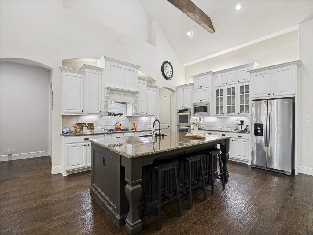 Modern kitchen with white cabinetry, stainless steel appliances, dark wood island with black stools, and hardwood flooring.