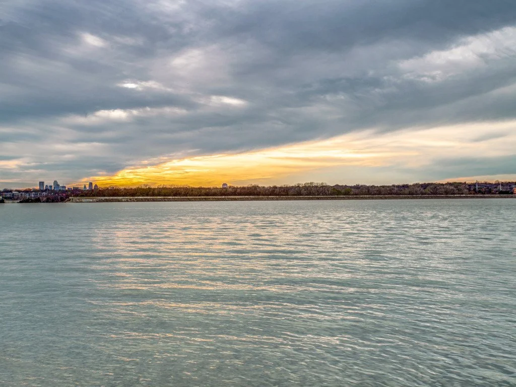 A sunset over a body of water with a city skyline in the distance and the sky filled with clouds.