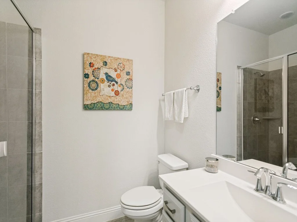 Bathroom with a white vanity, large mirror, white towel, toilet, shower with glass door, and wall art featuring a bird and flowers.