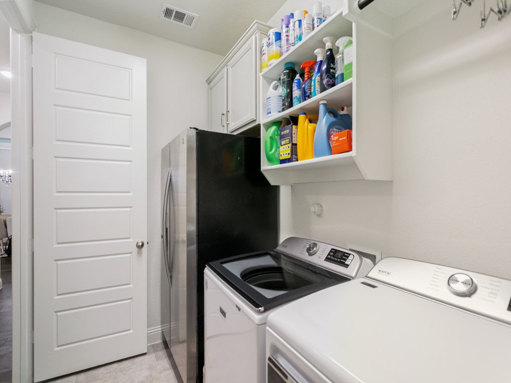 Laundry room with a white washing machine, a white dryer, a black refrigerator, white cabinets, and an open shelving unit with cleaning supplies.