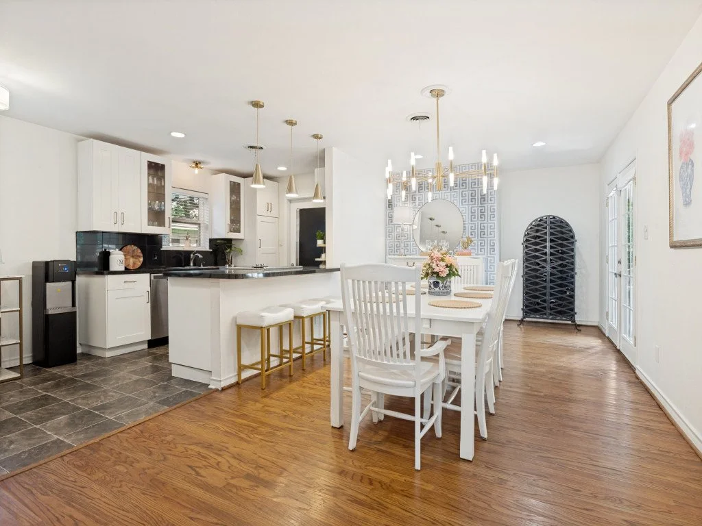 Open-concept kitchen and dining area with white cabinets, black countertops, a chandelier, and wooden flooring.