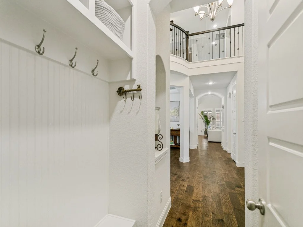 Bright hallway with wooden flooring, white walls, decorative lighting, and staircase with black railing leading to upper level.