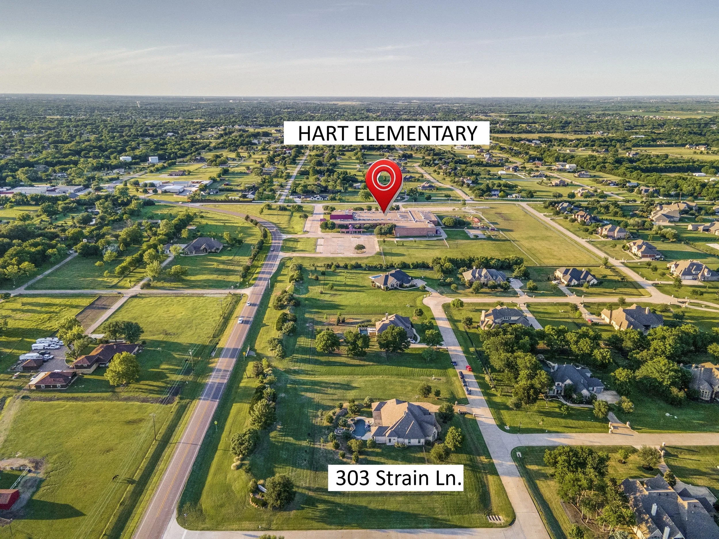 Aerial view of a residential neighborhood with houses and green lawns. A large building with a red roof is visible, marked with a red map pin labeled "HART ELEMENTARY." A road labeled "303 Strain Ln." runs through the neighborhood.
