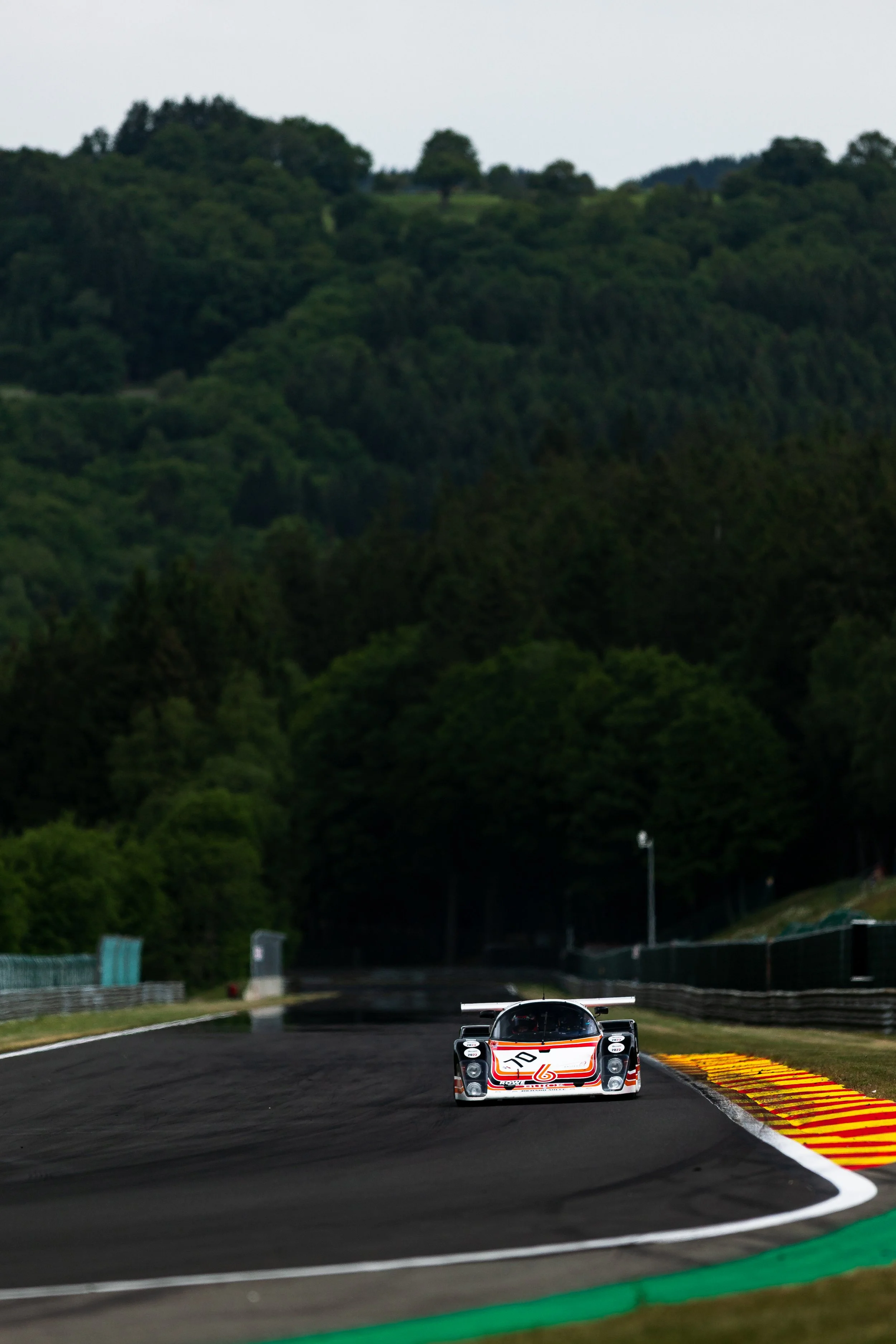A race car driving on a winding race track surrounded by green trees and hills. Peter Auto Spa Classic 2025. Legacy Outlaws Racing Team. Tiga GT286 Group C.