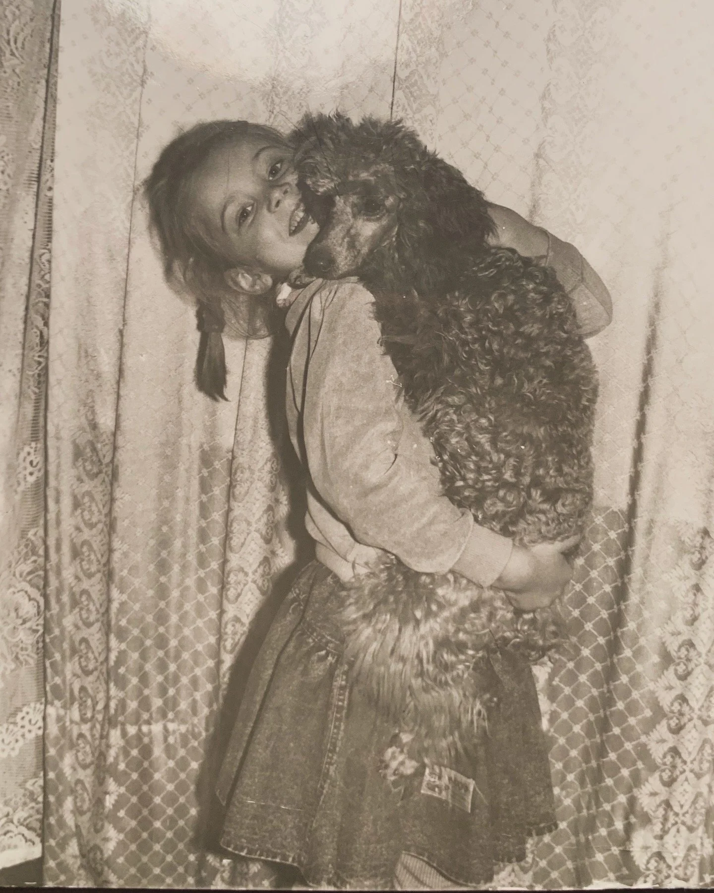 A young girl hugging a curly-haired dog on a patterned couch.