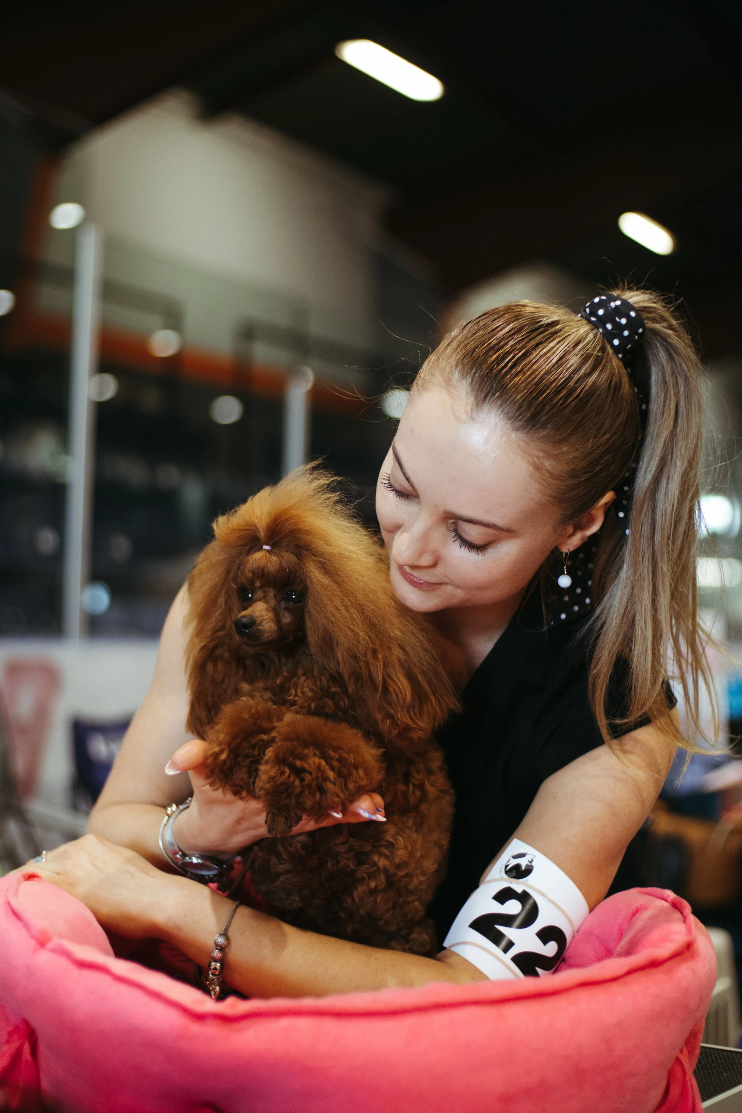 A woman holding a small brown poodle in an indoor setting.