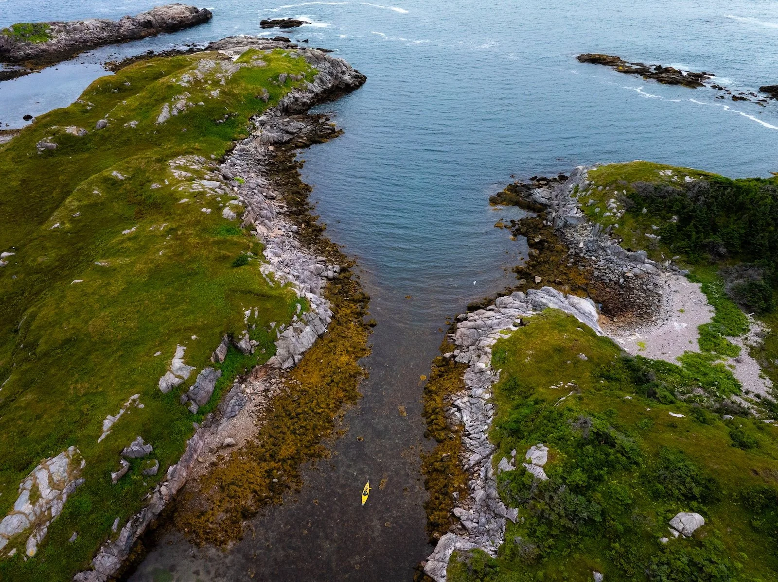Aerial view of a narrow inlet near Ramea, with rocky shores and green grassy areas, with a kayak in the water.