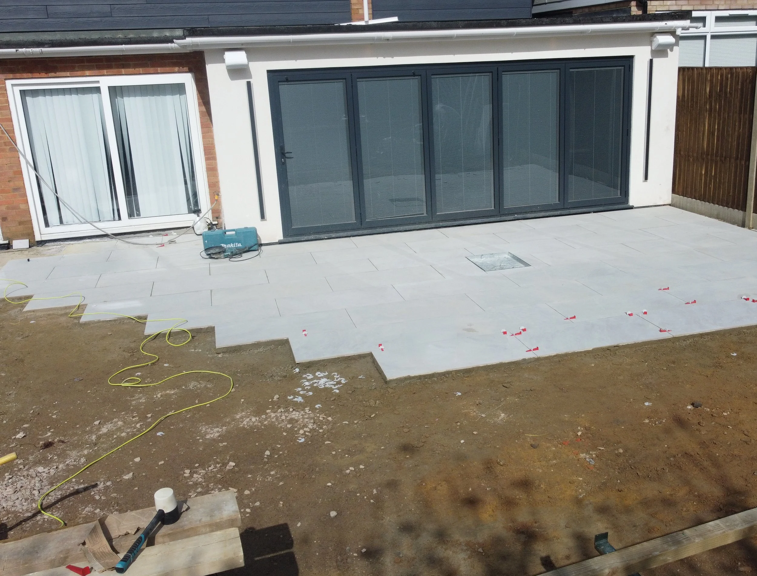 Unfinished patio with tiles and construction tools in front of a house with sliding glass doors.