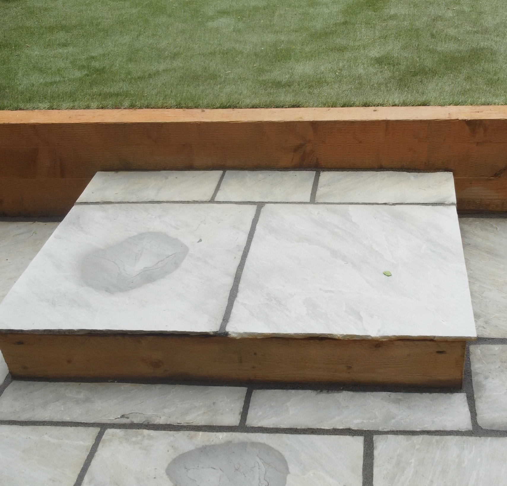 Close-up of a small soapstone step, part of a patio area with a wooden border, grass beyond.