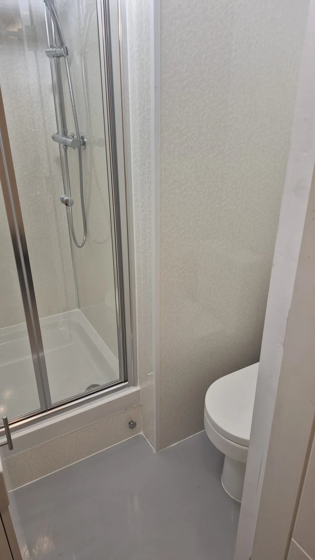 Small bathroom with a corner shower with glass doors and a handheld showerhead, and a toilet in the corner.