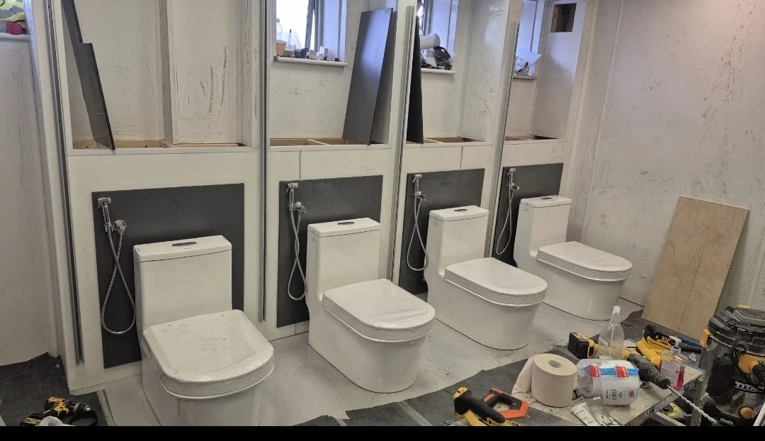 Four bathrooms under construction, each with a modern toilet and a wall-mounted hand shower, in a renovation site with tools and materials scattered around.