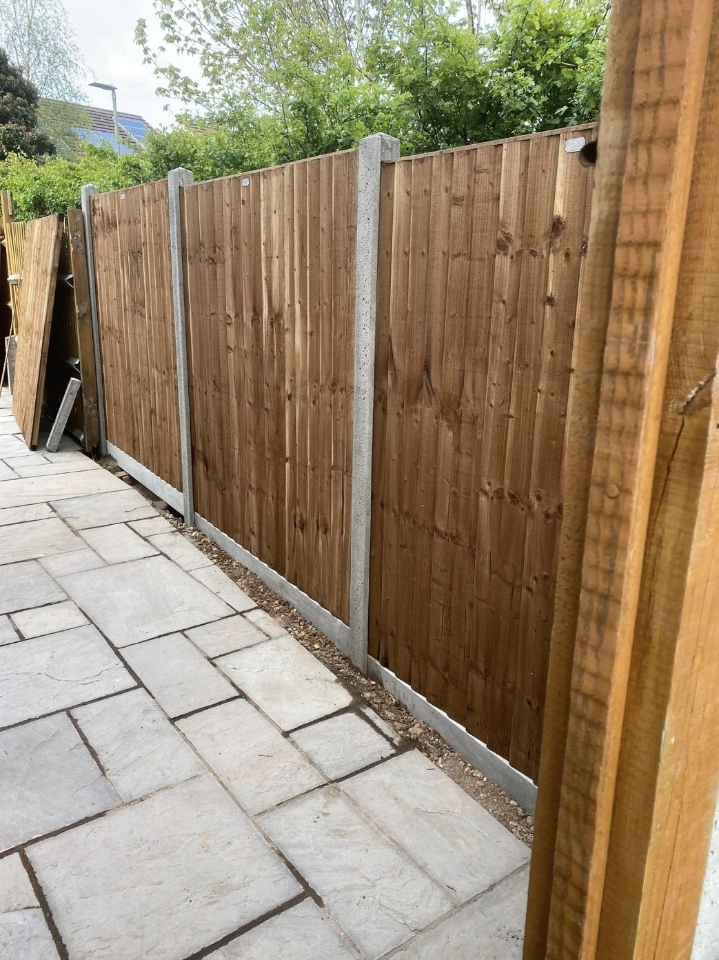 A newly installed wooden fence along a paved patio area, with some construction materials visible on the left side.