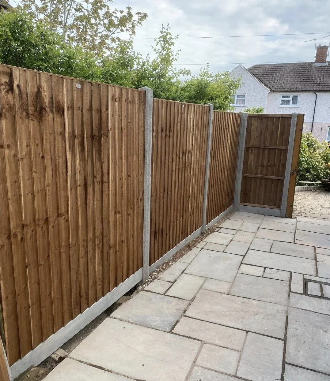 A backyard with a stone patio and a wooden fence with concrete posts and an access gate.