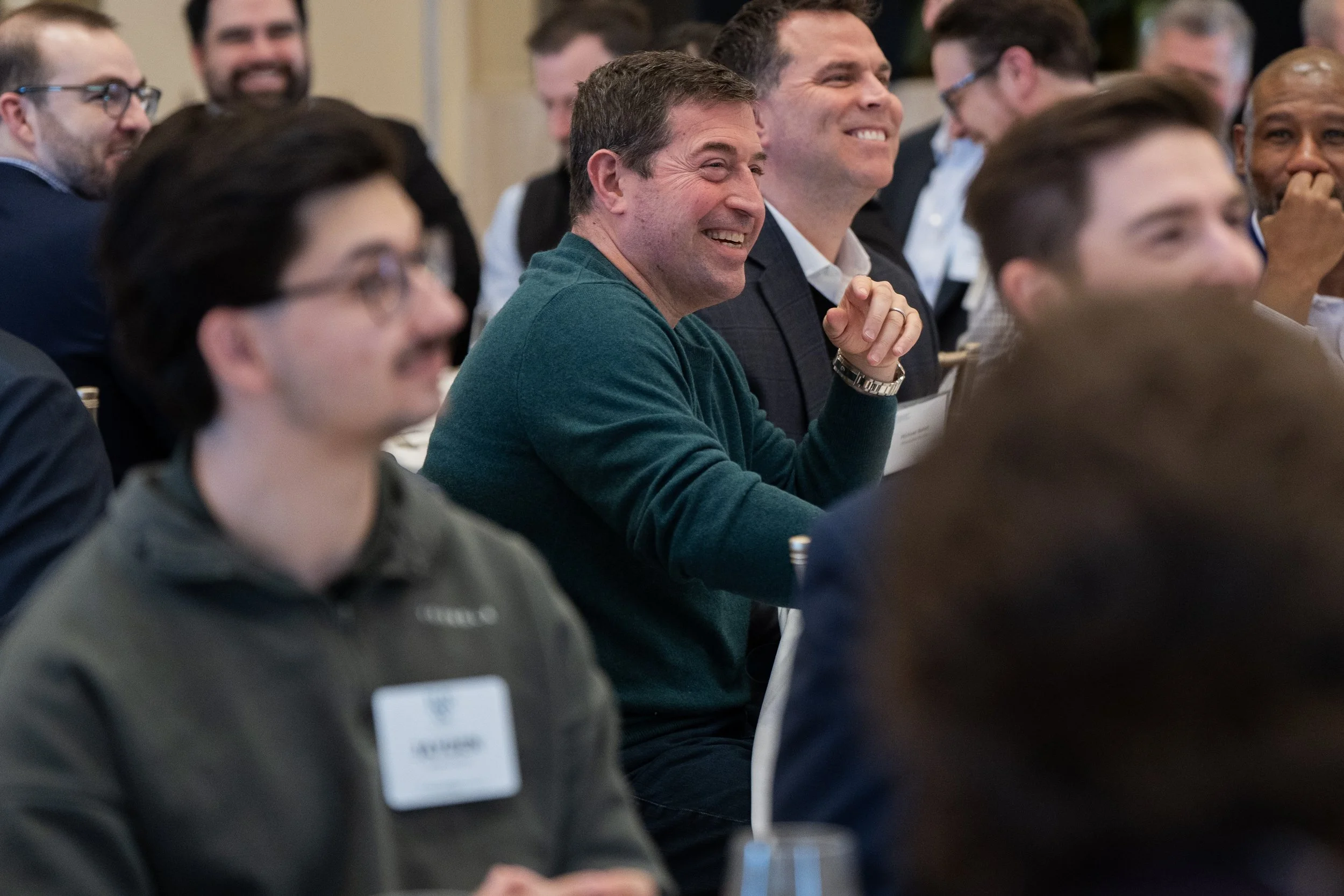 A group of people seated at a conference or seminar, smiling and listening attentively.