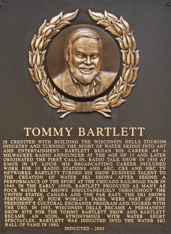 A bronze plaque features a detailed portrait of Tommy Bartlett surrounded by a laurel wreath. Below the portrait, text describes Bartlett's contributions to water ski sports, broadcasting career, and recognition in the Water Ski Hall of Fame.