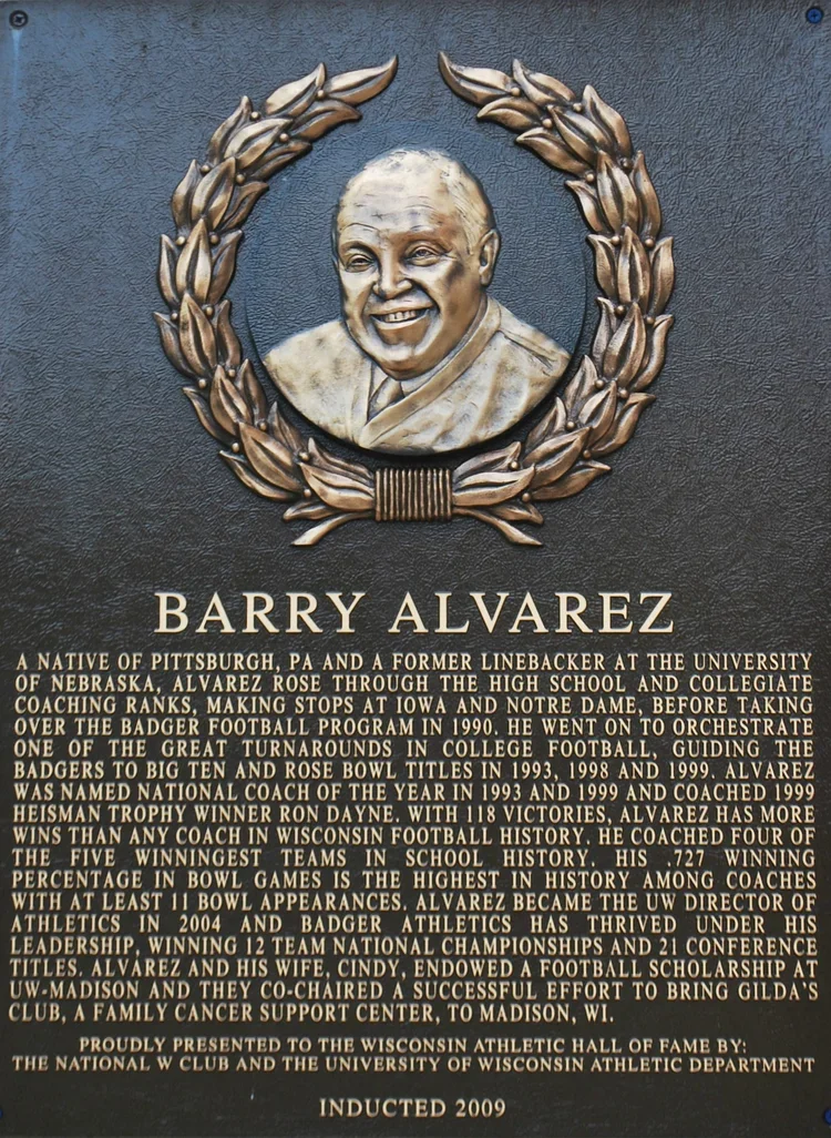 Plaque featuring a bronze portrait of Barry Alvarez surrounded by a football laurel wreath, with an inscription detailing his achievements in college football coaching and contributions to Wisconsin athletics, installed in 2009.