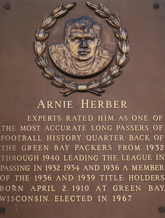 Plaque with a laurel wreath and a portrait of Arnie Herber, a football quarterback, with descriptive text about his career with the Green Bay Packers and personal details.