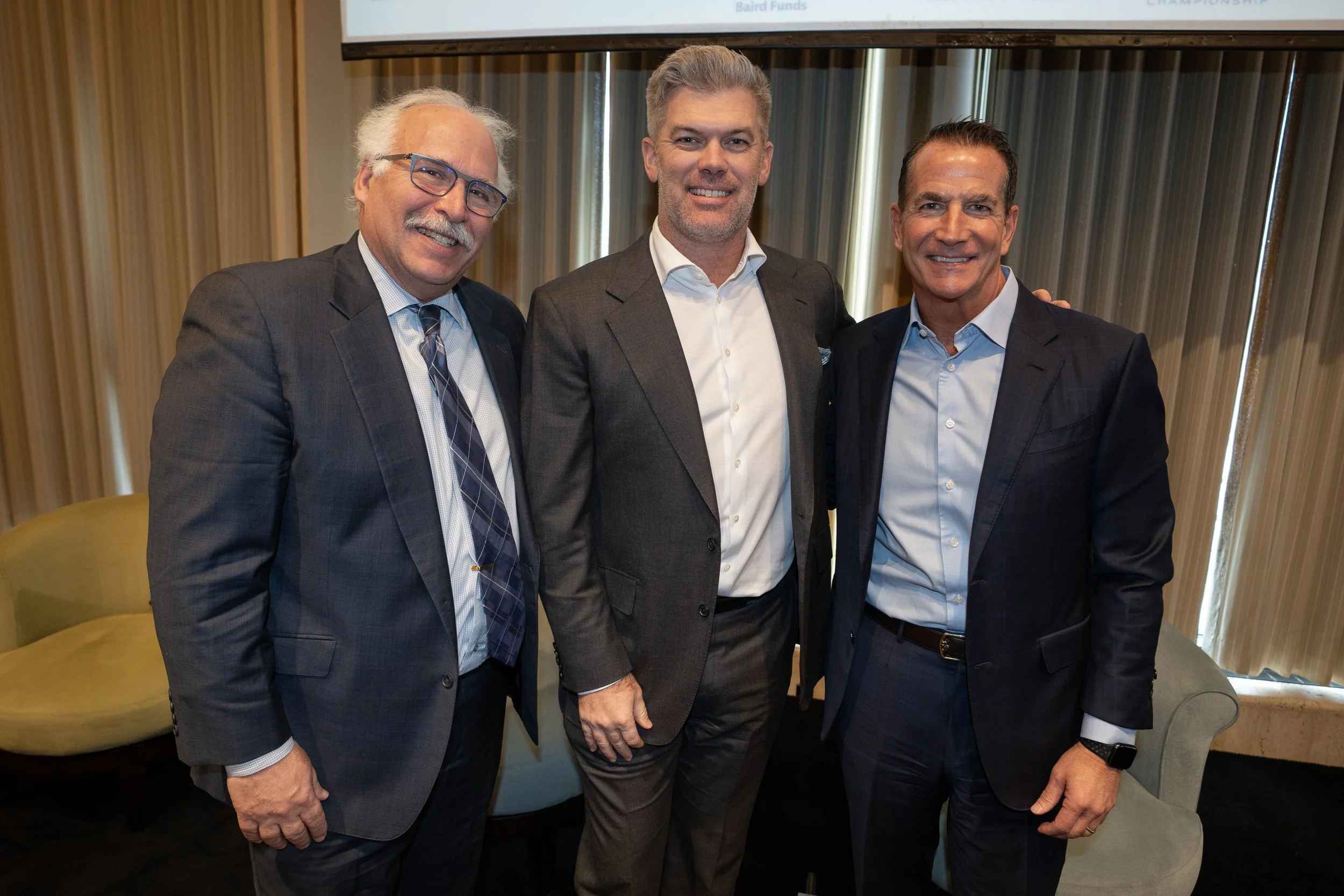 Three men in business suits standing together and smiling for a photo at an indoor event.