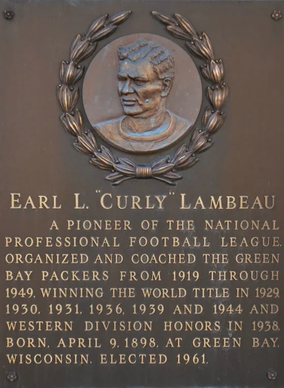 Plaque with a portrait of Earl L. Curly Lambeau and text describing his contributions to professional football, including organizing and coaching the Green Bay Packers, winning the 1929 World Championship, and his birth and death details.