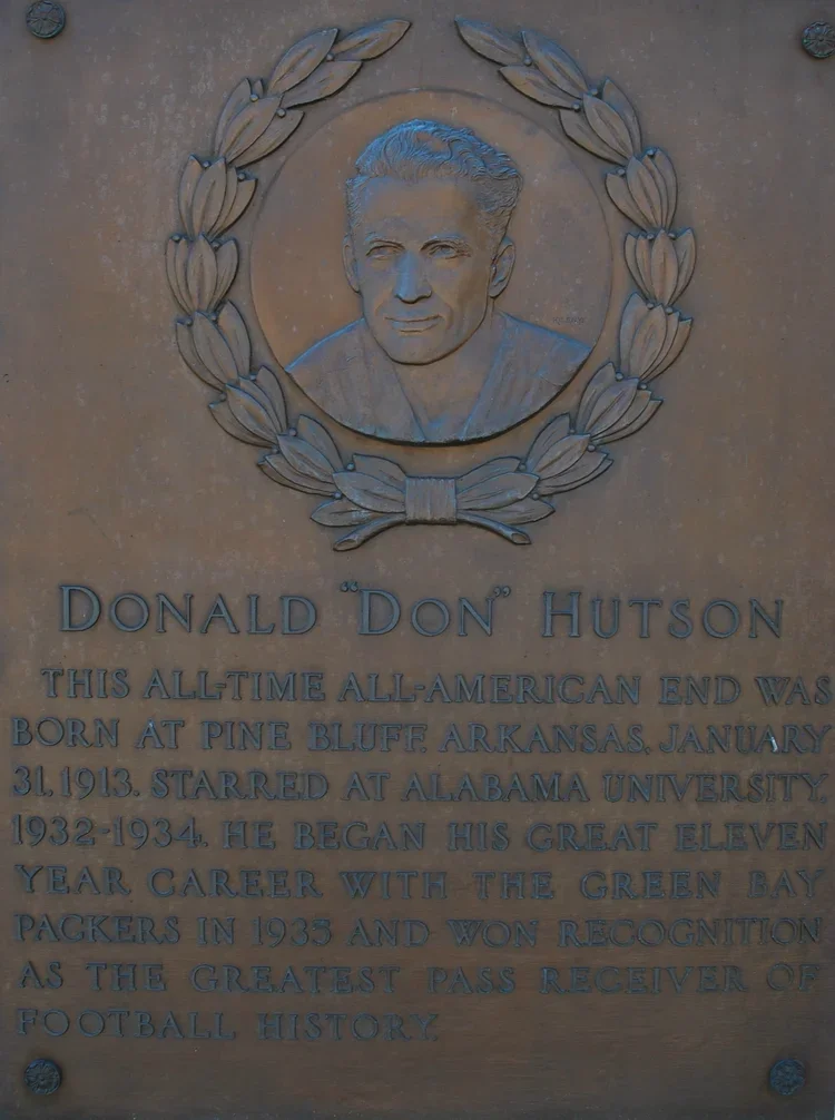 Plaque with a portrait of a man surrounded by a laurel wreath, dedicated to Donald 'Don' Hutson. The plaque details his birthplace in Pine Bluff, Arkansas, his birth date, his attendance at Alabama University, his career with the Green Bay Packers, and his recognition as a great football pass receiver.