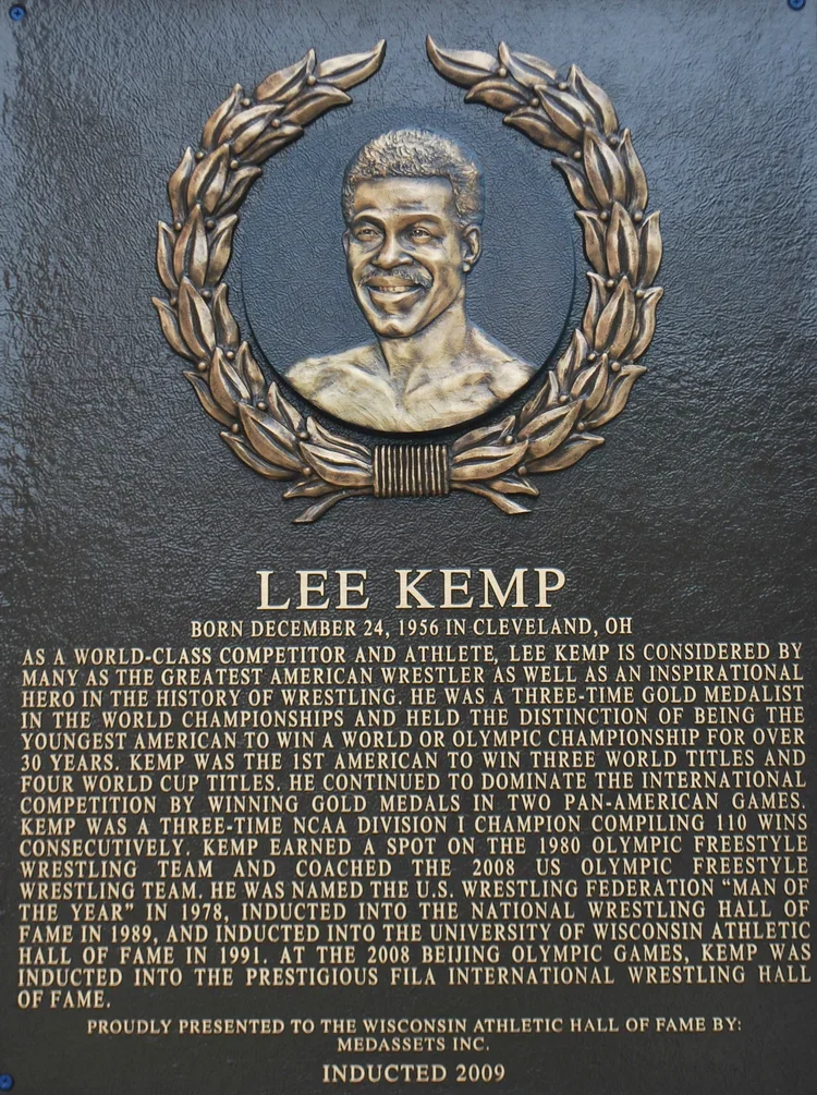 Bronze plaque featuring a relief portrait of Lee Kemp, a wrestler, with a laurel wreath and detailed biographical text about his achievements.