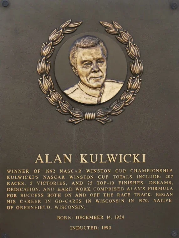 Plaque with an engraved portrait of Alan Kulwicki surrounded by a laurel wreath, and text describing his racing career and achievements.