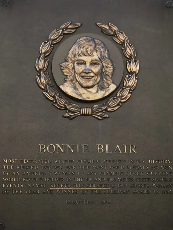 Plaque with a portrait of Bonnie Blair, a decorated Winter Olympic athlete, surrounded by a laurel wreath. The plaque describes her achievements, including five gold medals, world records, and awards.