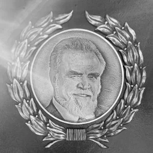 Black-and-white photograph of a man with a beard and short hair, framed by a circular laurel wreath.