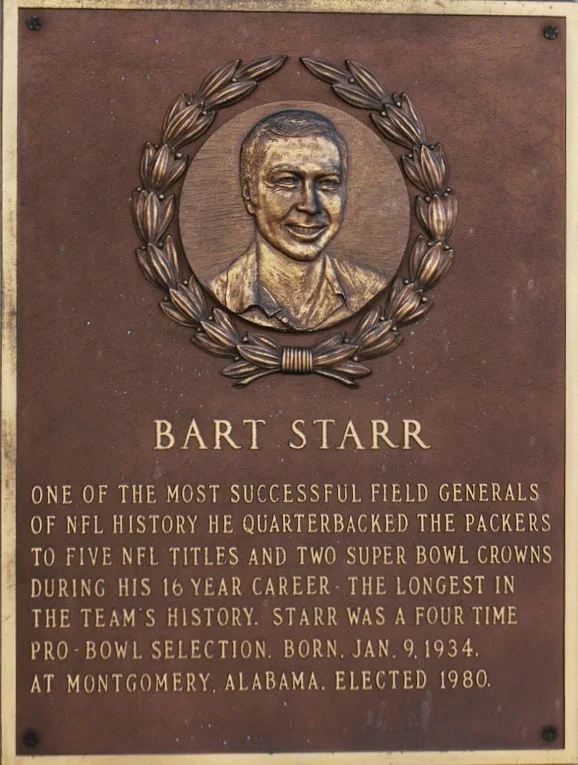 Plaque with a bronze portrait of Bart Starr surrounded by a laurel wreath. Text describes Bart Starr as a successful NFL quarterback for the Green Bay Packers, with numerous titles and accomplishments, born January 9, 1934, elected in 1980, from Montgomery, Alabama.