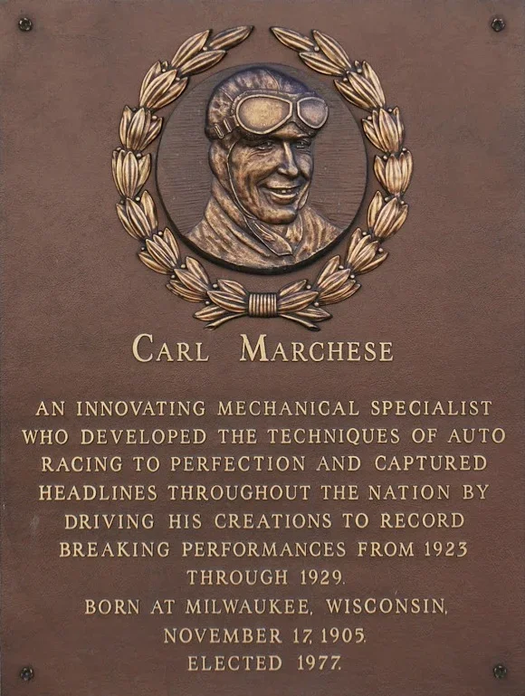 Bronze plaque with an engraved portrait of Carl Marchese wearing goggles, surrounded by a laurel wreath. The plaque provides a brief biography highlighting his achievements as an innovative mechanical specialist in auto racing, born in Milwaukee, Wisconsin, on November 17, 1905, and elected in 1977.