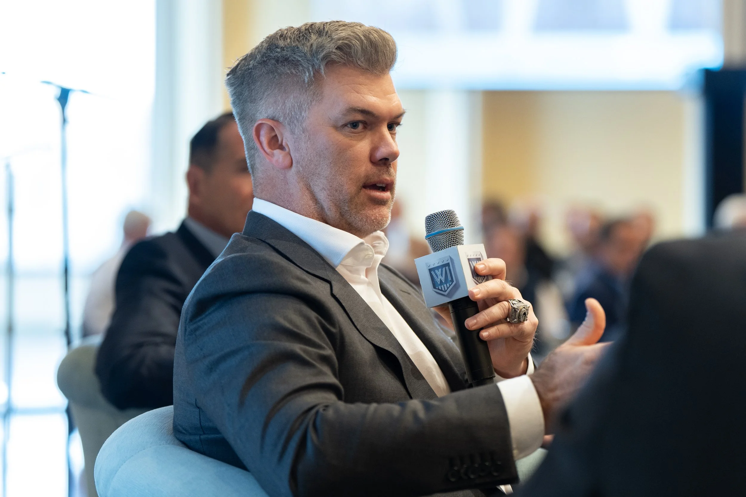 Man in gray suit speaking into a microphone during a conference or panel discussion.