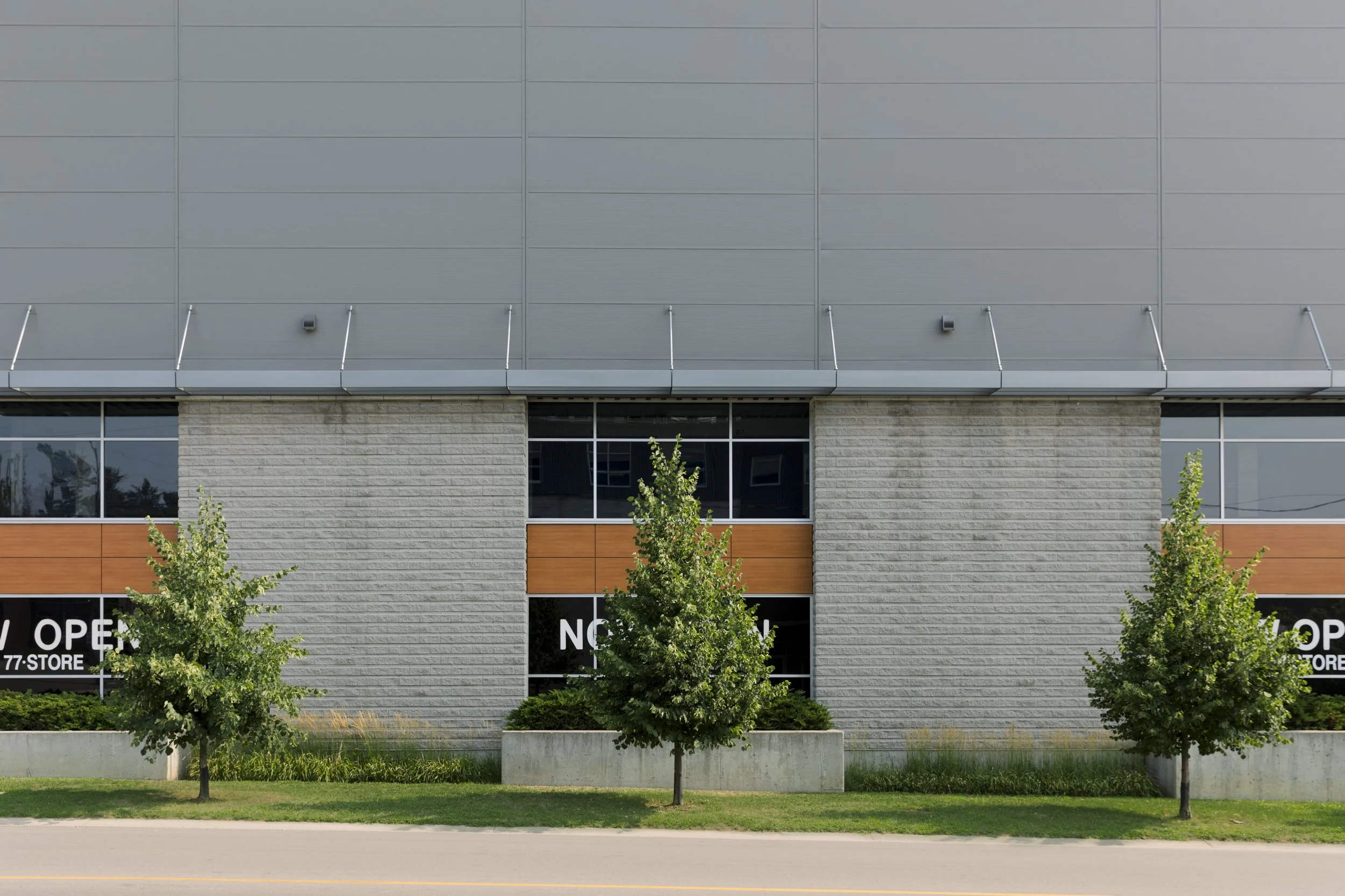 Facade of a modern commercial building with large windows, gray panels, and three small trees planted in front.