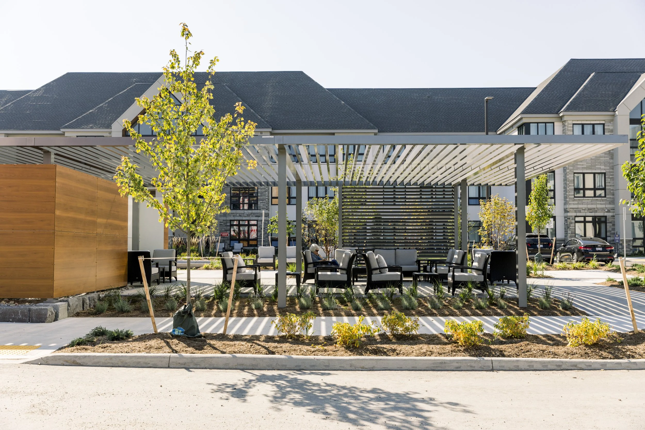 Outdoor seating area with chairs and tables under a modern pergola in a residential complex.