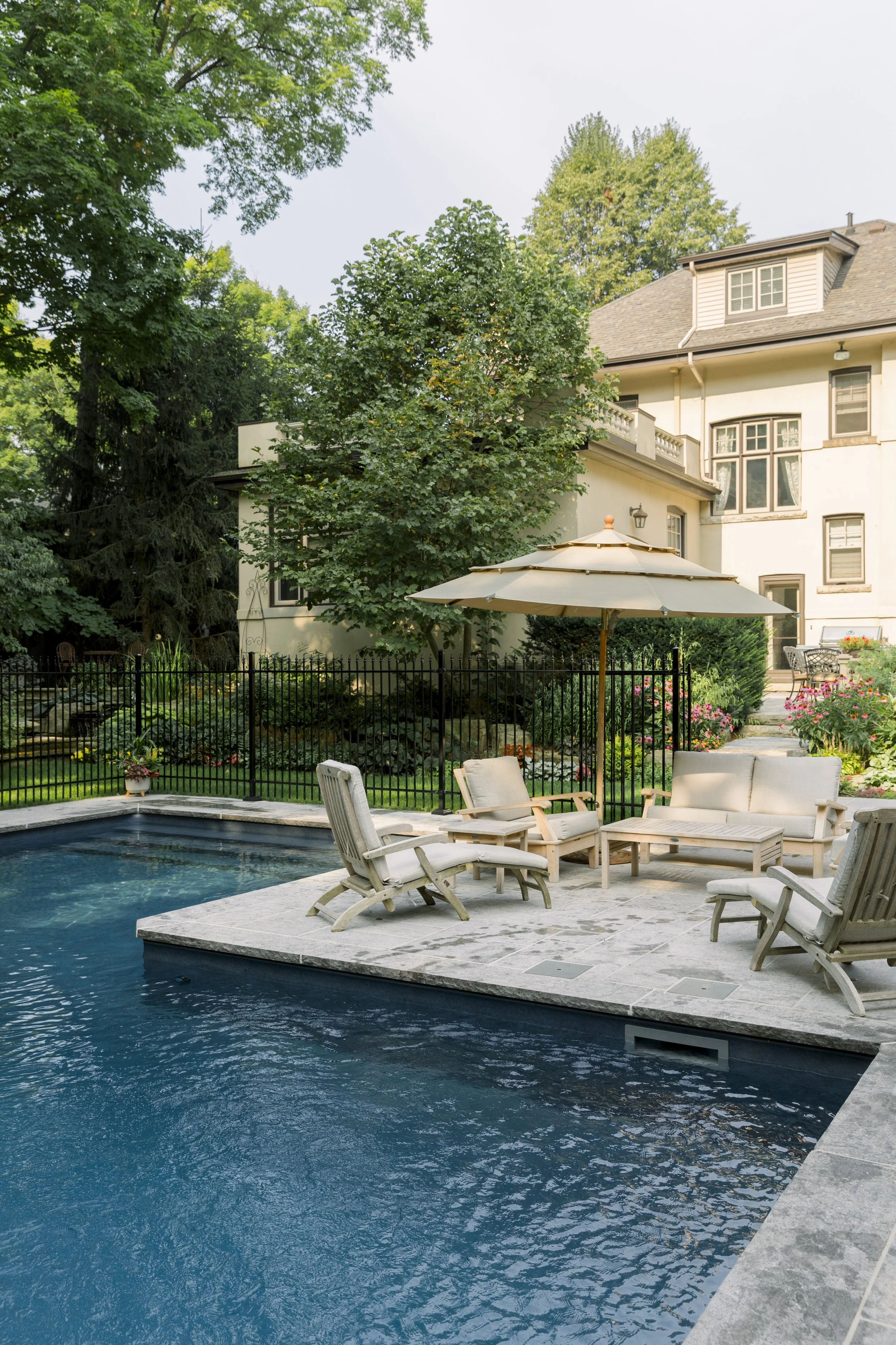 A backyard with a swimming pool, outdoor furniture, and lush greenery.