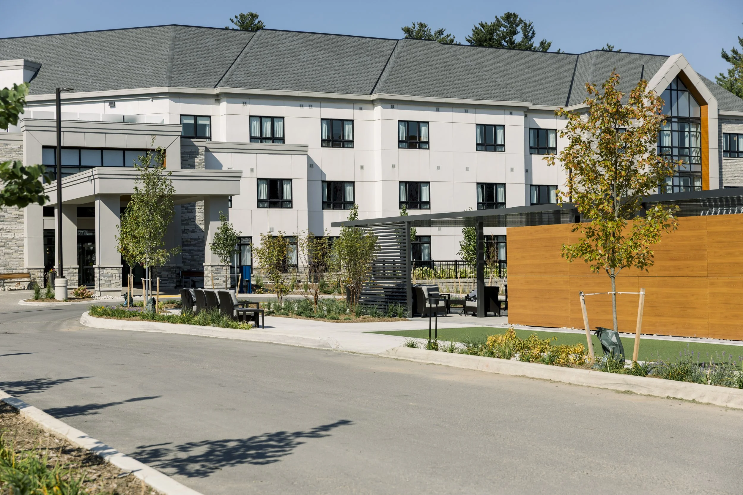 Modern apartment complex with landscaped outdoor area, benches, trees, and a wooden privacy wall.