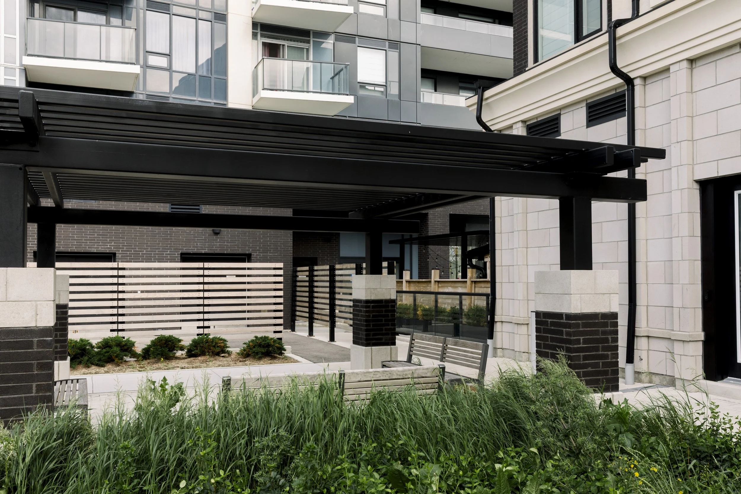 Modern apartment complex with black and white facade, patio with benches, greenery, and a small garden.