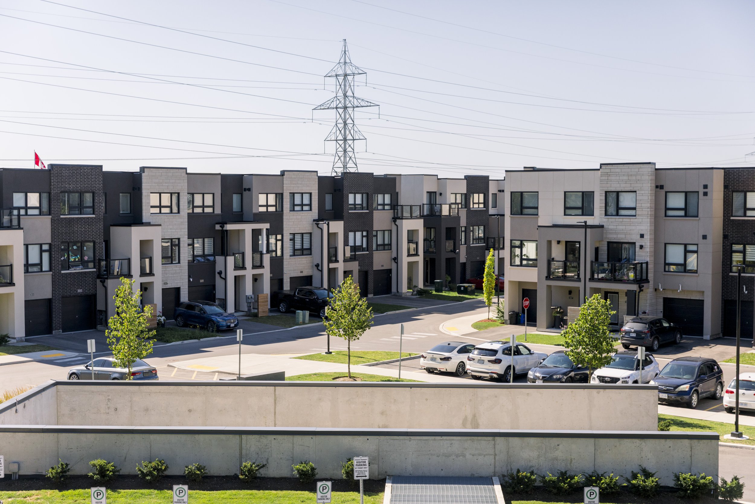 Modern multi-story apartment complex with parking lot, trees, and a concrete wall in the foreground.