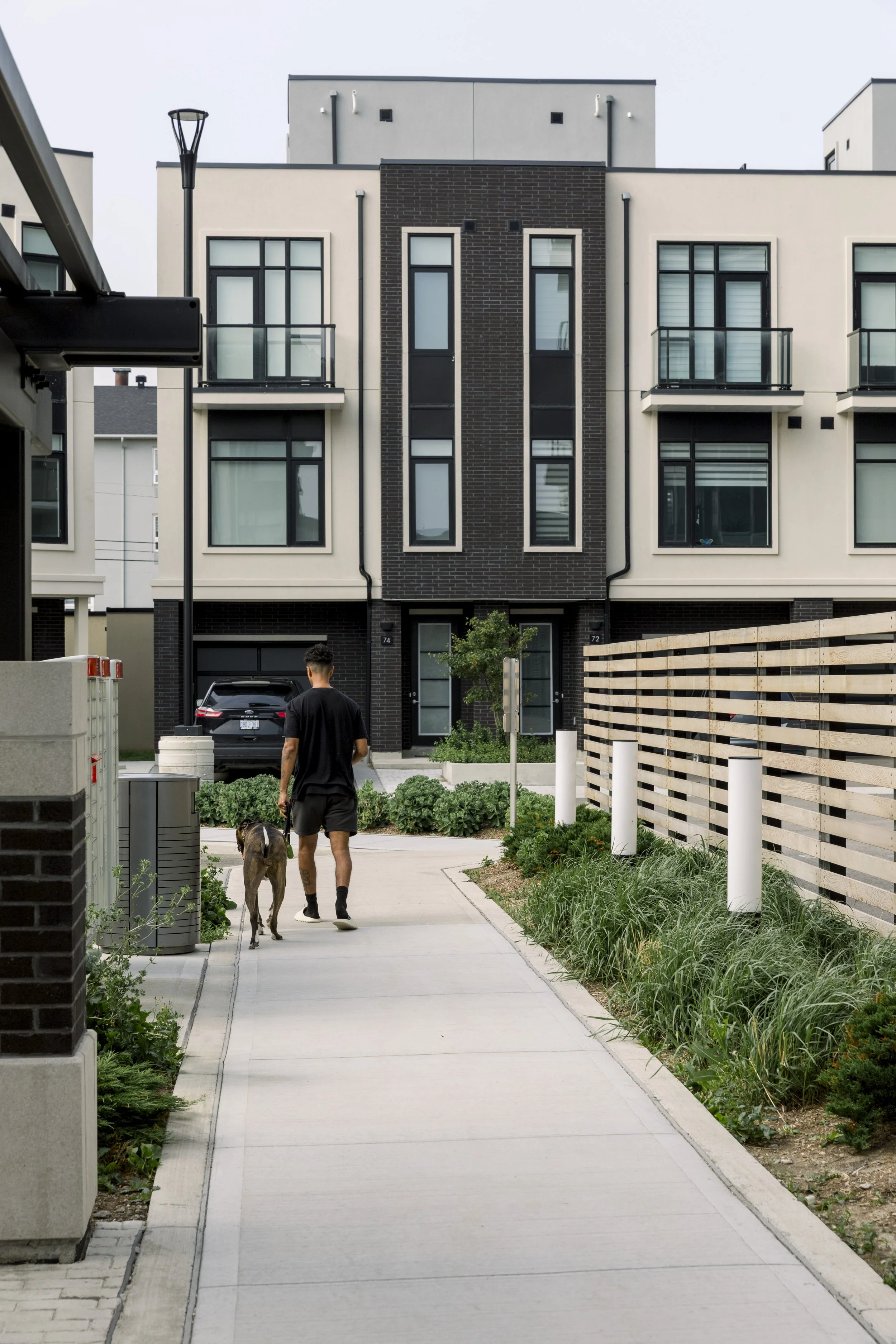 A man walking a dog along a sidewalk in front of modern apartment buildings with balconies and landscaping.